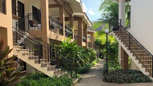 A building with multiple balconies, a central pathway, and surrounding greenery.