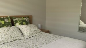 A neatly made bed with a floral patterned bedspread and pillows, a wooden headboard, and a wall-mounted painting.