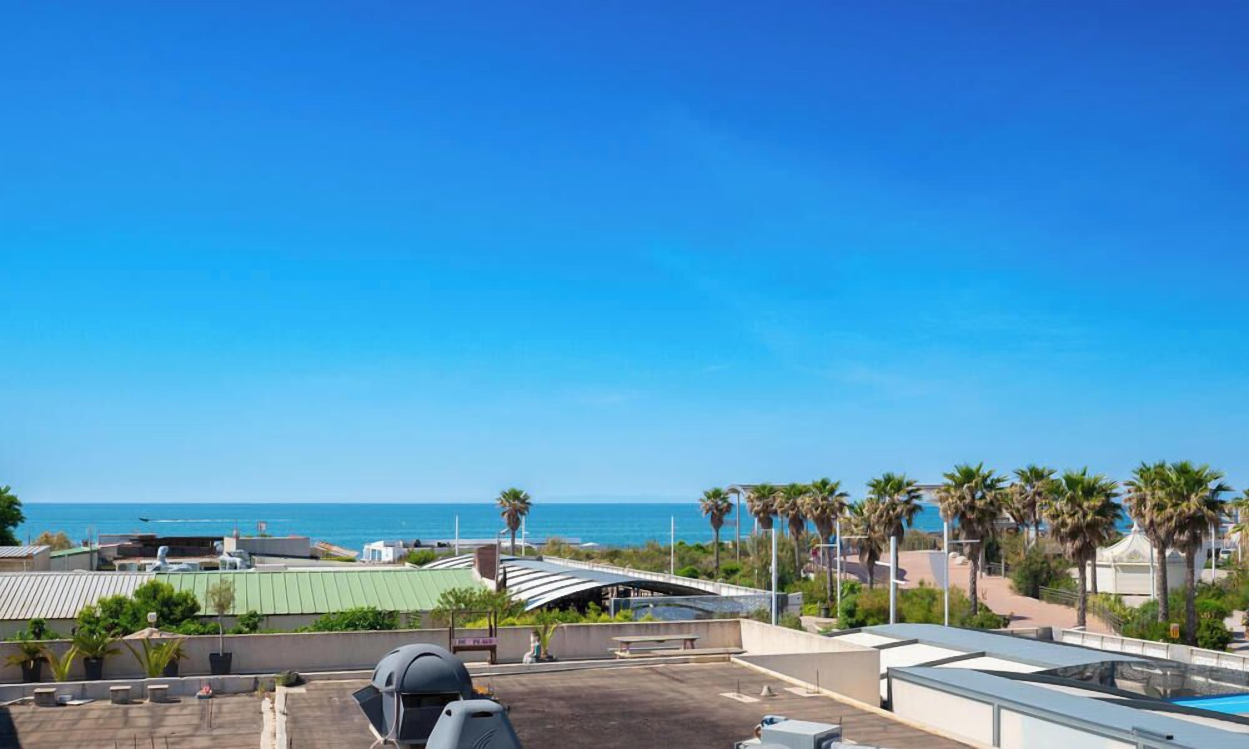 Terraza en la azotea con vistas al mar, palmeras y un espacio cubierto con asientos.