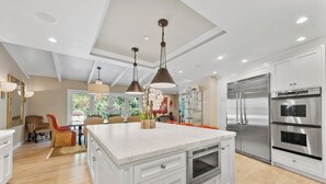 Uma cozinha moderna com armários brancos, eletrodomésticos de aço inoxidável e iluminação pendente.