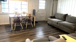 Una habitació amb taula de dinar, cadires, sofà, televisió i una porta.