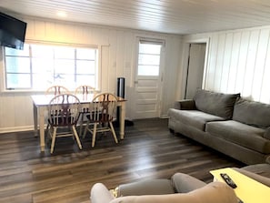 A room with a dining table, chairs, a sofa, a TV, and a door.