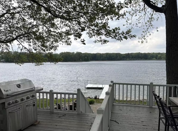 A deck with a grill, a dock, and a view of a lake.