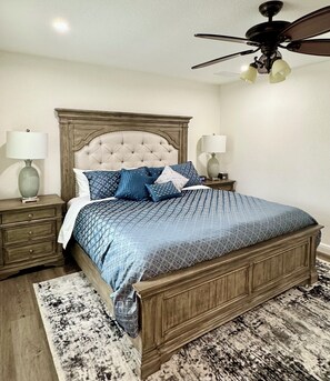 A bedroom with a wooden bed, two bedside tables, a ceiling fan, and a patterned rug. - DFW Executive Globe Life, ATT Stadium, Six Flags FIFA World Cup Home Arlington (Arlington)