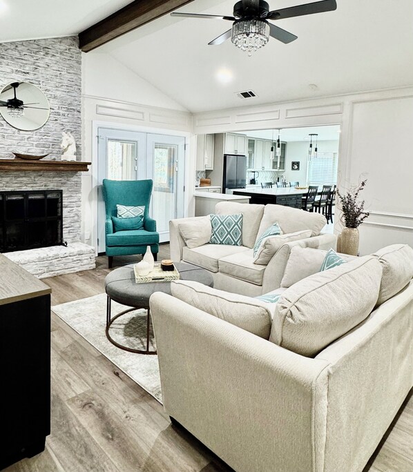 A living room with a fireplace, teal armchair, beige sofa, and a dining area in the background. - DFW Executive Globe Life, ATT Stadium, Six Flags FIFA World Cup Home Arlington (Arlington)