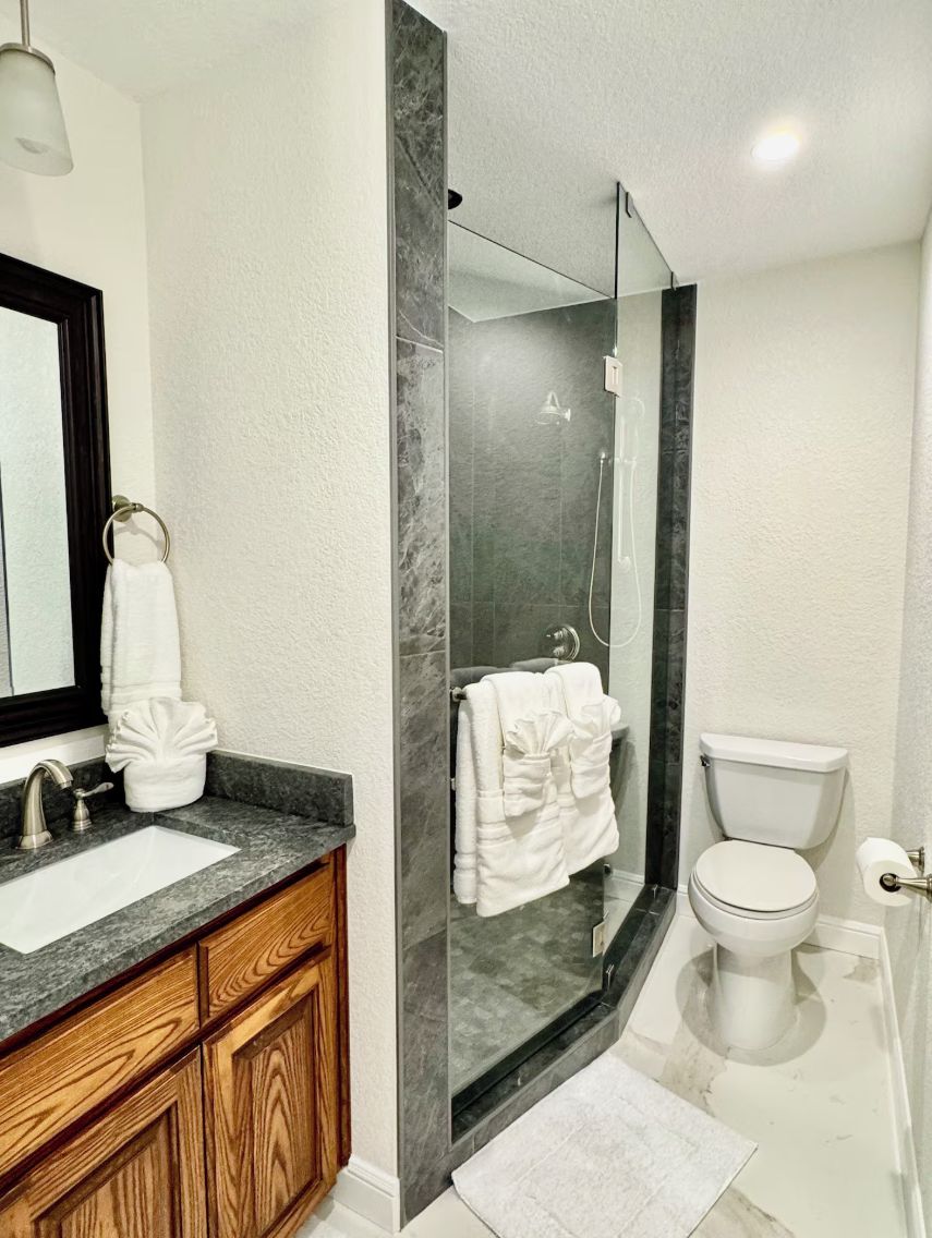 A modern bathroom with a marble shower, a wooden vanity, and a white toilet.