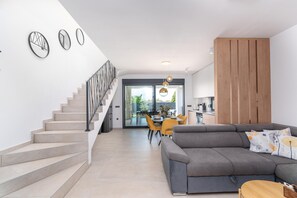 A modern living room with a grey sofa, wooden panel wall, staircase, and dining area with yellow chairs. - 6-person Home With 3 En-suites (Novigrad)