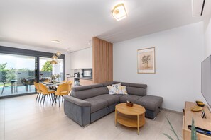 A modern living room with a sectional sofa, dining table, and chairs, a wooden coffee table, and a kitchen in the background. - 6-person Home With 3 En-suites (Novigrad)