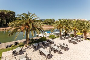 Una terraza con mobiliario exterior, palmeras y vistas a un cuerpo de agua.