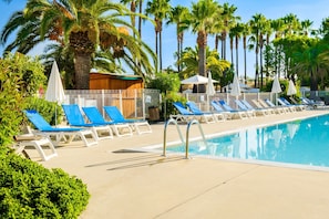 Zona de piscina amb gandules, palmeres i cel blau.
