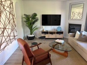 Ein modernes Wohnzimmer mit Sofa, Glastisch, Topfpflanze, Fernseher und einer Wanddekoration.