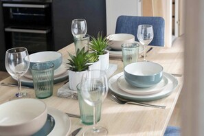 Ruokapöytä on katettu lautasilla, kulhoilla, laseilla ja siinä on myös ruukussa oleva kasvi.