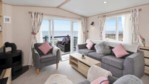 Una sala de estar acogedora con chimenea, sofás grises y vista al mar.