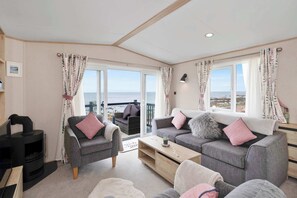Ein gemütliches Wohnzimmer mit Kamin, grauen Sofas und Meerblick.