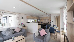 Una sala de estar moderna con sofá, sillón y mesa de centro, un comedor con mesa y sillas, y una cocina con electrodomésticos.