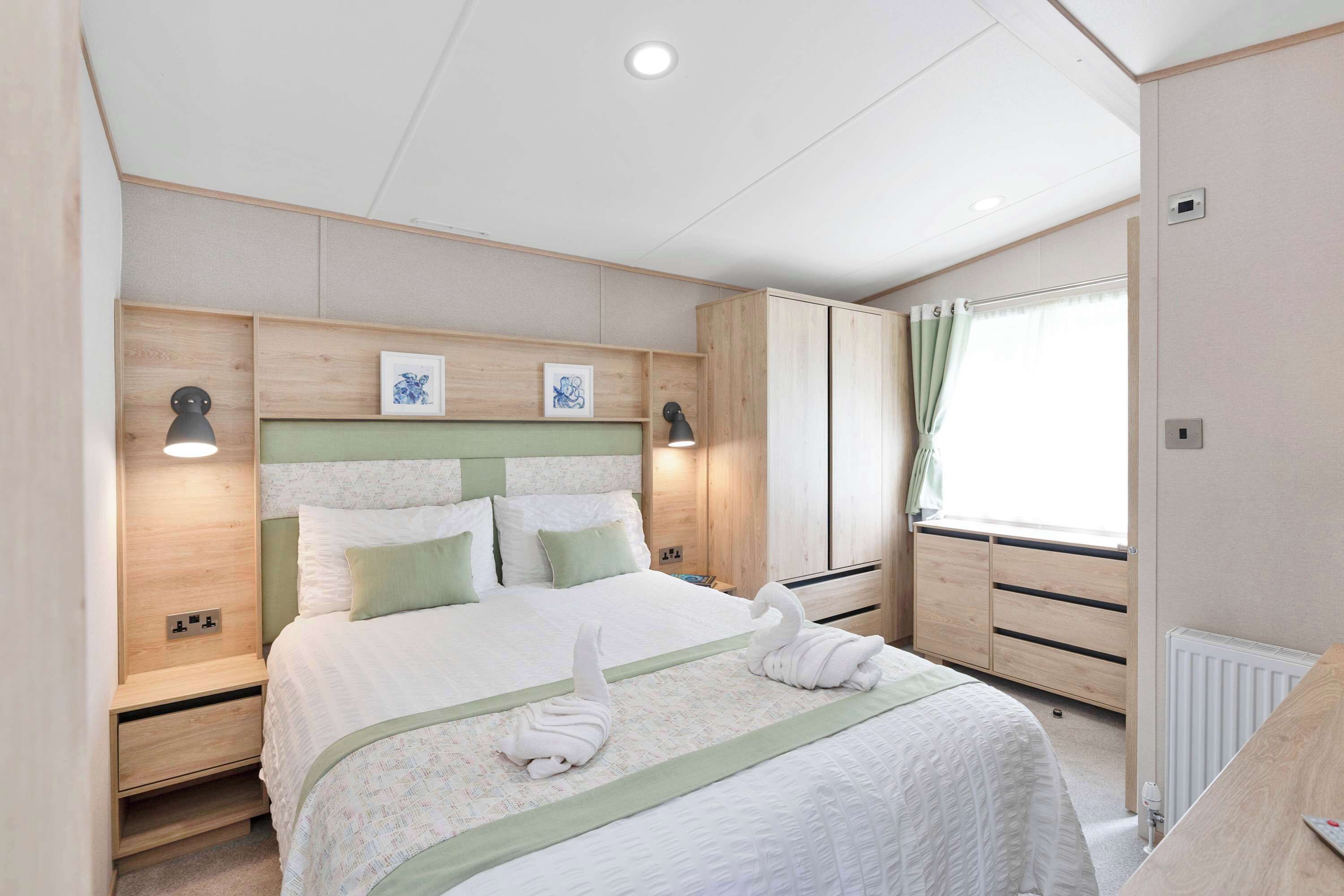 Een slaapkamer met een bed, nachtlampjes, een dressoir, een radiator en een raam met gordijnen.