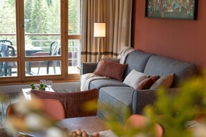 A cozy room with a grey sofa, a table with a vase, and a window with curtains. - Mountain View Retreat With Balcony for 8 (Araches-la-Frasse)
