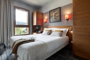 A hotel room with a large bed, wooden headboard, a painting on the wall, and a window with curtains. - Mountain View Retreat With Balcony for 8 (Araches-la-Frasse)