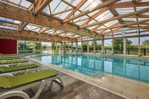 An indoor swimming pool with wooden beams, clear glass walls, and green lounge chairs. - Elegant 4-pax Apartment With River View (Courseulles-sur-Mer)