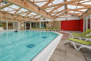 An indoor swimming pool with a wooden ceiling and glass panels, surrounded by lounge chairs. - Elegant 4-pax Apartment With River View (Courseulles-sur-Mer)