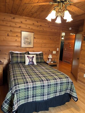 A wooden-paneled bedroom with a bed, a nightstand, a lamp, and a framed picture on the wall.