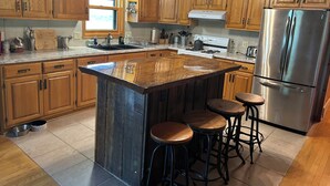 Una cocina con armarios de madera, un refrigerador de acero inoxidable, una isla grande con taburetes y un ventilador de techo.