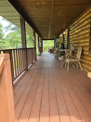 A wooden deck with a railing, a table with chairs, and a view of trees.