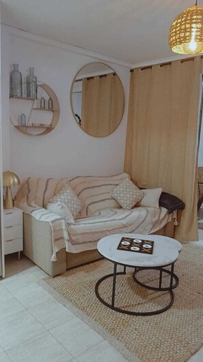Un salon avec un canapé, un miroir rond, une petite table et un luminaire suspendu.