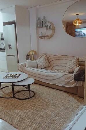 Un salon comprenant un canapé, une table basse ronde, une étagère murale décorative et un téléviseur.