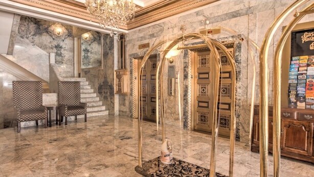 Un hall d’entrée en marbre, agrémenté d’un magnifique escalier, d’un comptoir de réception et d’un lustre.