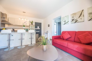 A modern living space with a kitchen, a red sofa, and a round table with a plant. - Lecci Apartment With Outdoor Pool (Lecci)