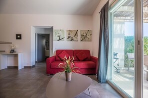 A modern living room with a red sofa, a potted plant on a round table, and artwork on the wall. - Lecci Apartment With Outdoor Pool (Lecci)