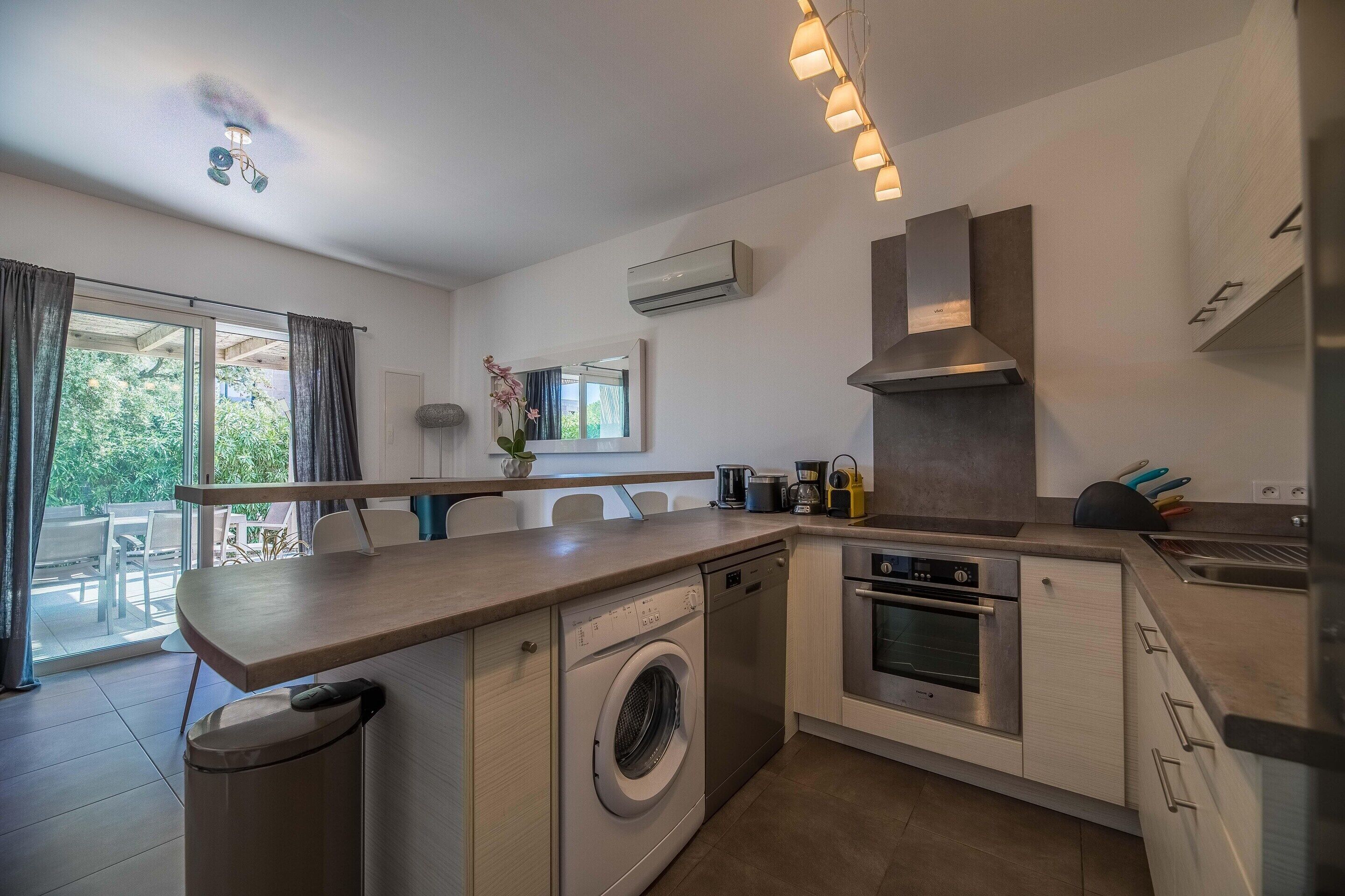 A modern kitchen with a built-in washing machine, oven, and a large window.