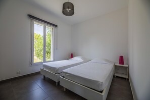 A bedroom with two beds, a window, and a nightstand with a lamp. - Lecci Apartment With Outdoor Pool (Lecci)