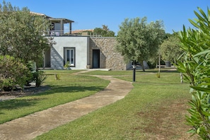 A modern building with a stone facade, a paved pathway, and surrounding greenery. - Lecci Apartment With Outdoor Pool (Lecci)