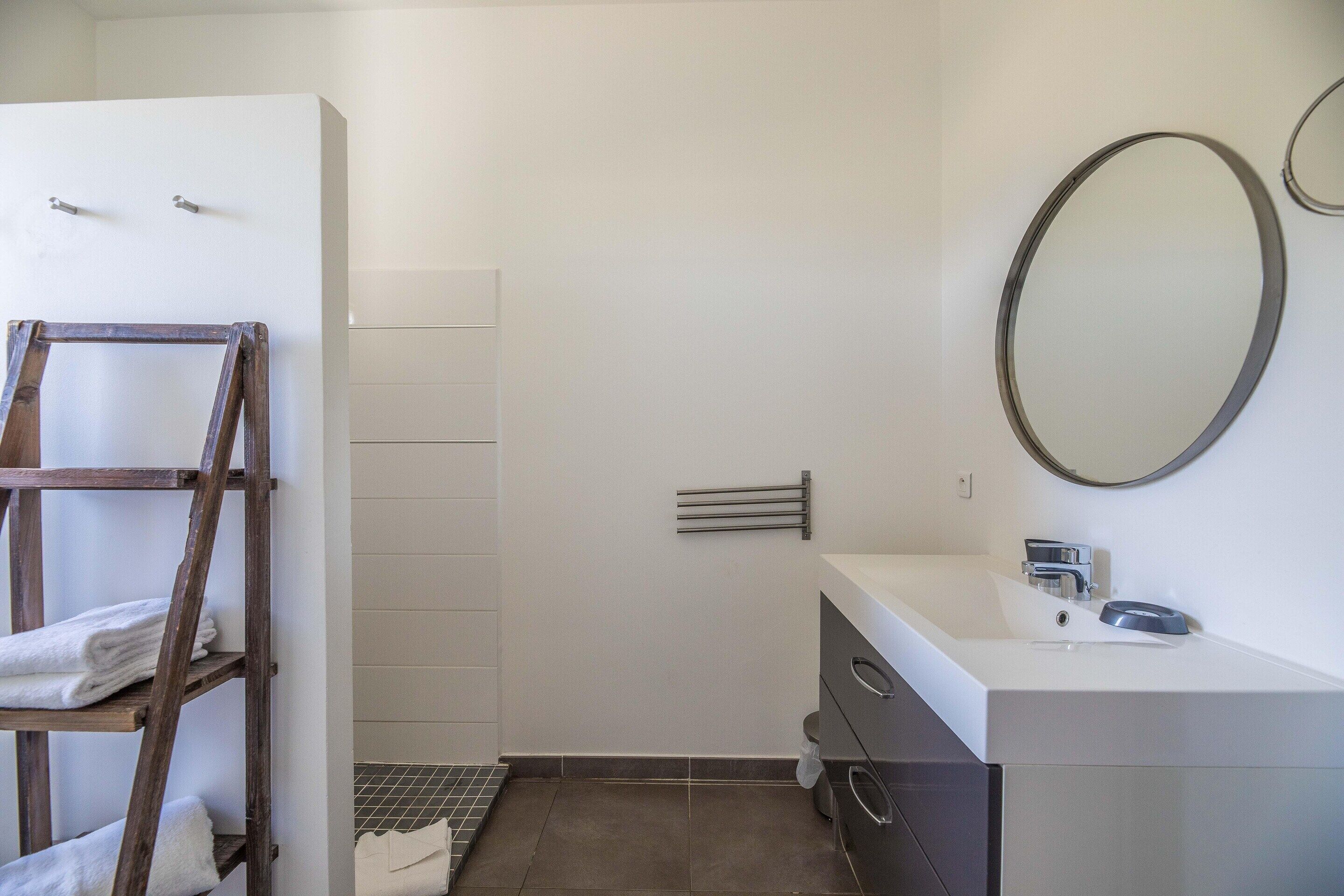 A bathroom with a white sink, a mirror, a towel rack, and a shower area.