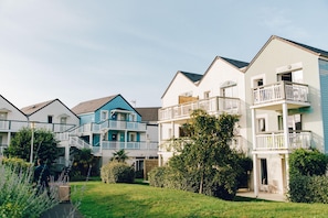 A row of multi-story residential buildings with balconies, a lawn, and a pathway. - Courseulles Family Apartment for 6 (Courseulles-sur-Mer)