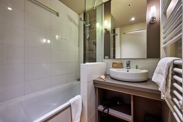 A modern bathroom with a bathtub, a sink, a mirror, and a towel rack. - Courseulles Family Apartment for 6 (Courseulles-sur-Mer)