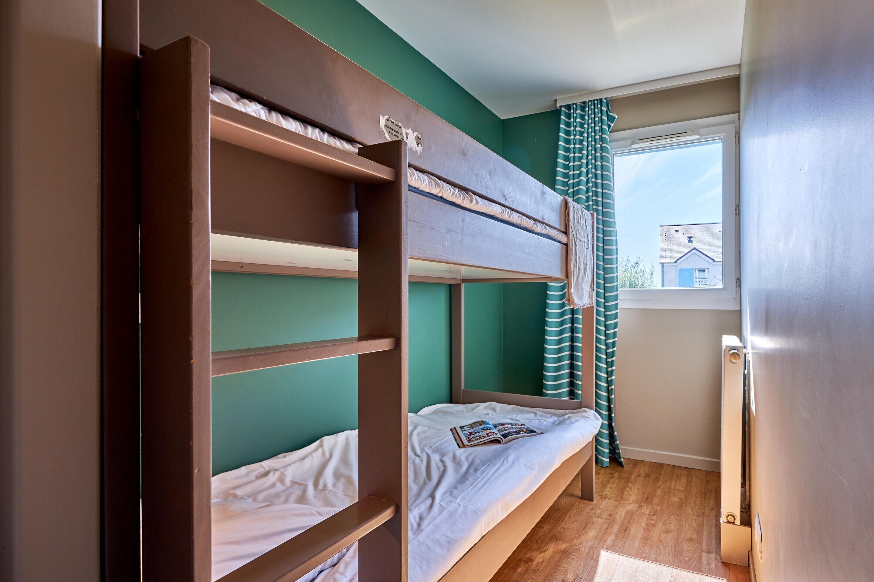 A bunk bed room with a window, a radiator, and a striped curtain.