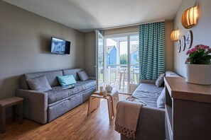 A modern living room with a grey sofa, a small wooden table, and a TV mounted on the wall. - Courseulles Family Apartment for 6 (Courseulles-sur-Mer)
