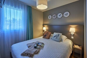 A neatly made bed with a pillow, a bedside lamp, and a small table with a book. - Courseulles Family Apartment for 6 (Courseulles-sur-Mer)