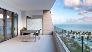 A balcony with a dining table and chairs, a glass railing, and a view of the ocean and resort area. - Beautiful location offers  white-sand beaches, gourmet dining and  infinity pool (Cancun)