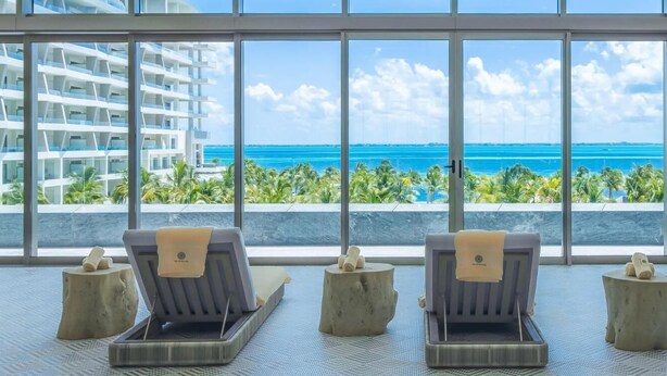 A room with large windows, a view of the ocean, and three sun loungers with towels. - Beautiful location offers  white-sand beaches, gourmet dining and  infinity pool (Cancun)