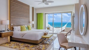 A hotel room with a bed, a desk, a chair, a large mirror, a ceiling fan, and a view of the ocean through large windows. - Beautiful location offers  white-sand beaches, gourmet dining and  infinity pool (Cancun)