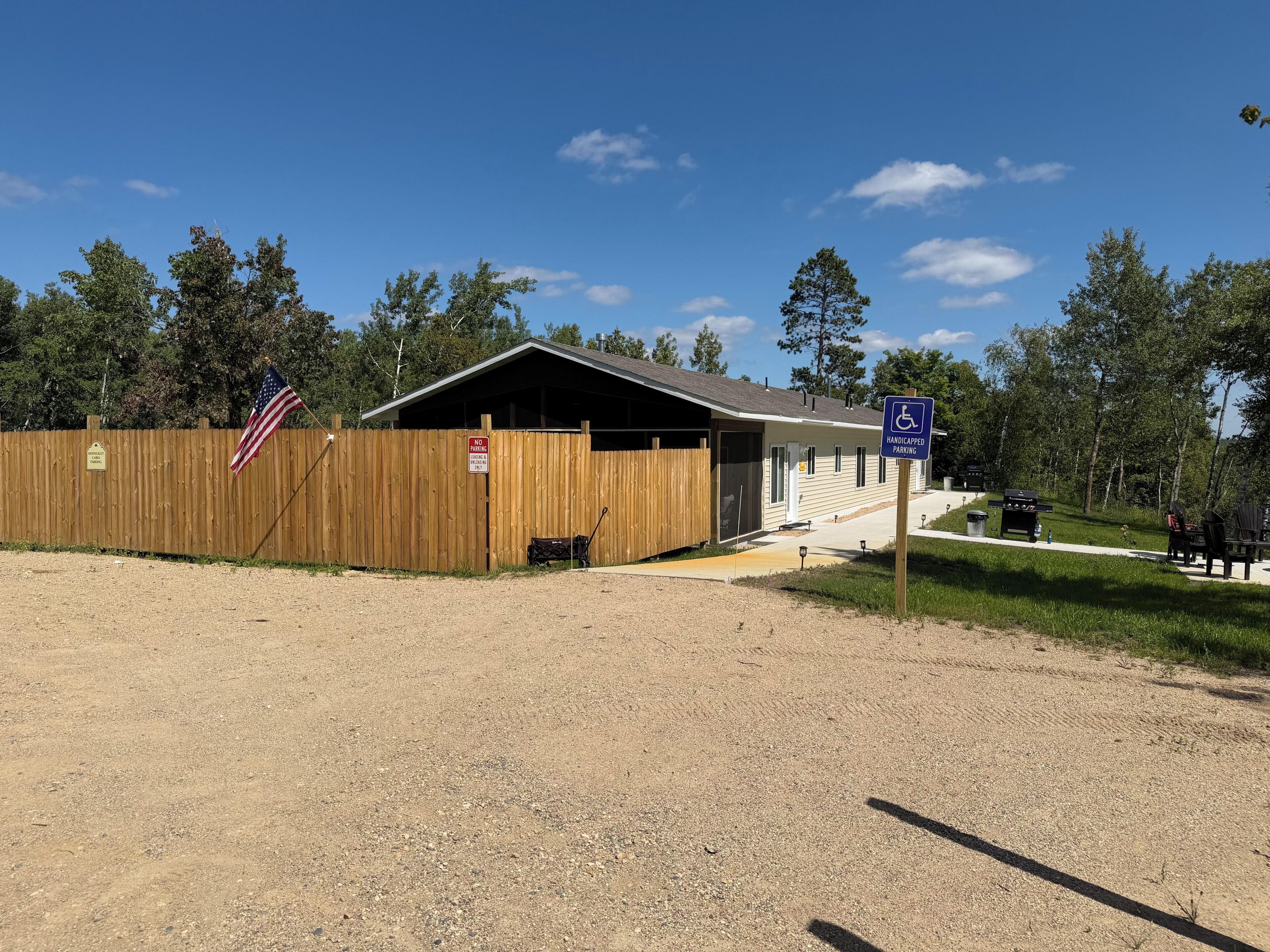 A building with a covered entrance, a handicapped parking sign, and a wooden fence with an American flag.