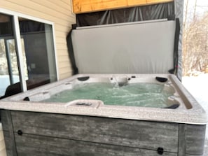 A hot tub with a wooden deck and a sliding glass door.