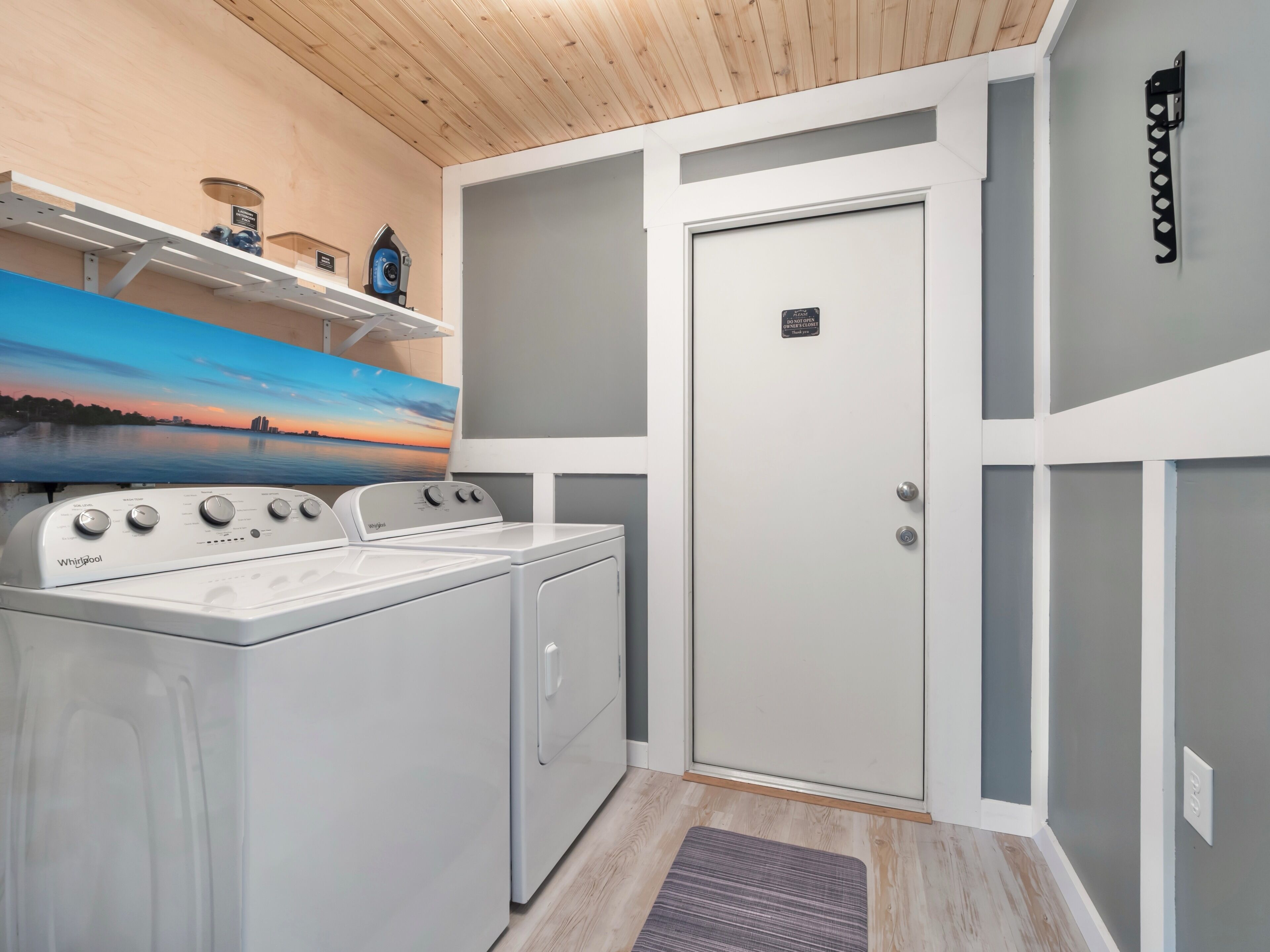 Una lavanderia con lavatrice e asciugatrice Whirlpool, una porta con il cartello 'Non Disturbare' e uno scaffale con oggetti.