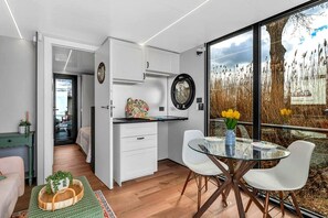 A modern kitchen with white cabinets, a glass dining table, and a view of tall grasses through a large window.