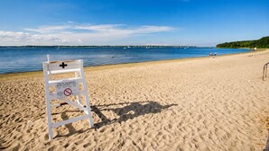Een strand met een redersbord, helderblauw water en verre boten.