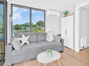 A modern living room with a grey sofa, a white coffee table, and a view of a marina through large windows.